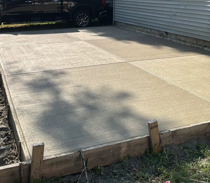 New concrete garage pad poured beside a house, jointed and still in timber forms