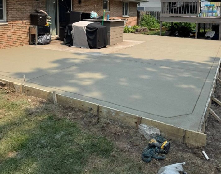 Large broom-finished concrete patio behind a brick house, forms still in place
